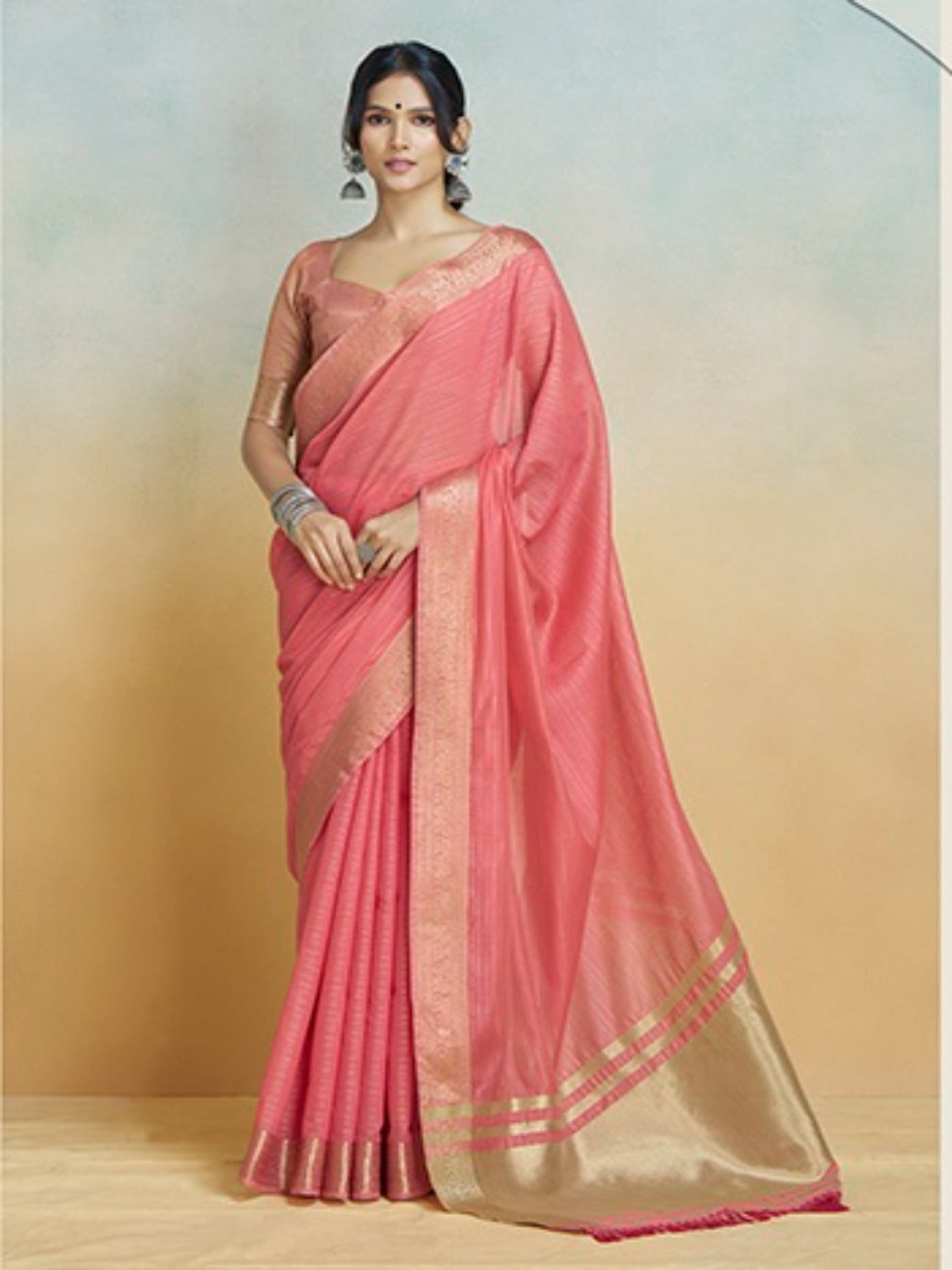 Woman wearing a pink saree with a gold border against a gradient background